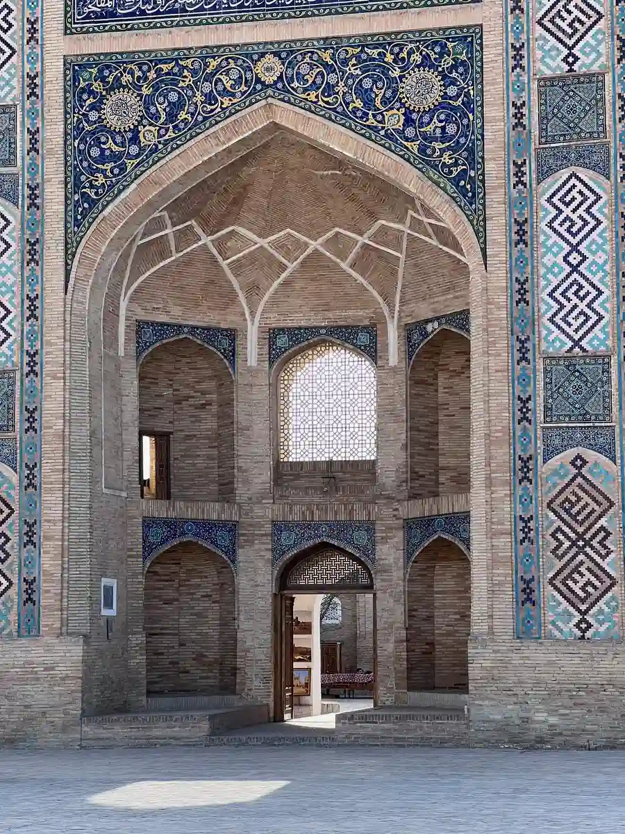 Ornately tiled entrance portal of a historic Bukhara madrasah with an arched brick ceiling